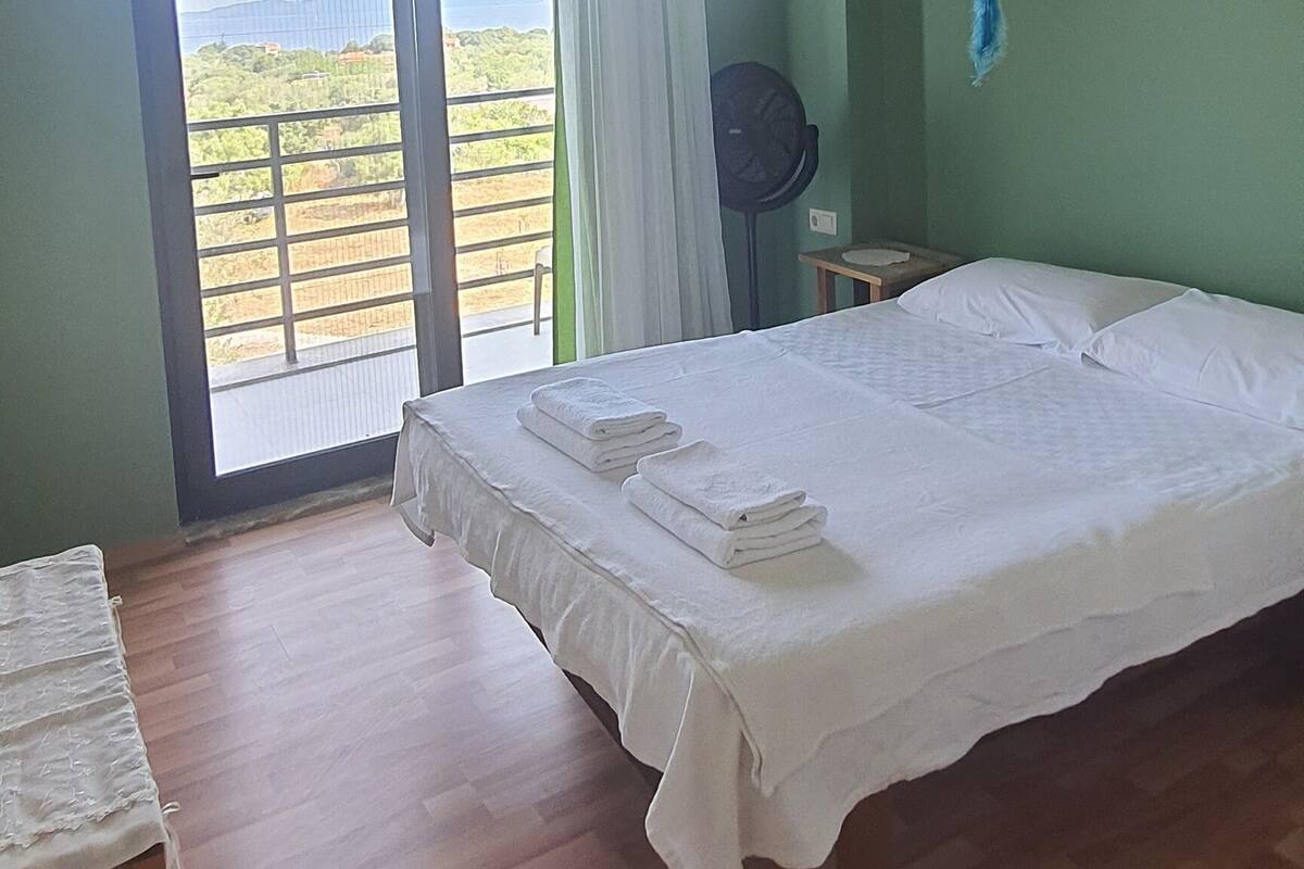 Ein Schlafzimmer mit einem großen Bett, Holzboden, Blick durch ein Fenster und einem Deckenventilator.