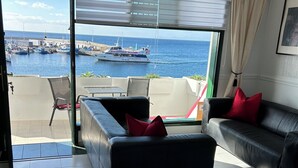 A modern living room with a black leather sofa, a red pillow, and a view of the sea and boats through large windows. - Pearl apartment - incredible view - in front of the ocean (Tías)