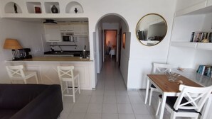 A modern kitchen with white cabinetry, a central island, and a dining area with white chairs and a wooden table. - Pearl apartment - incredible view - in front of the ocean (Tías)