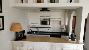 A compact kitchen with white cabinets, a black countertop, a microwave, and a sink. There are two white chairs at the counter. - Pearl apartment - incredible view - in front of the ocean (Tías)