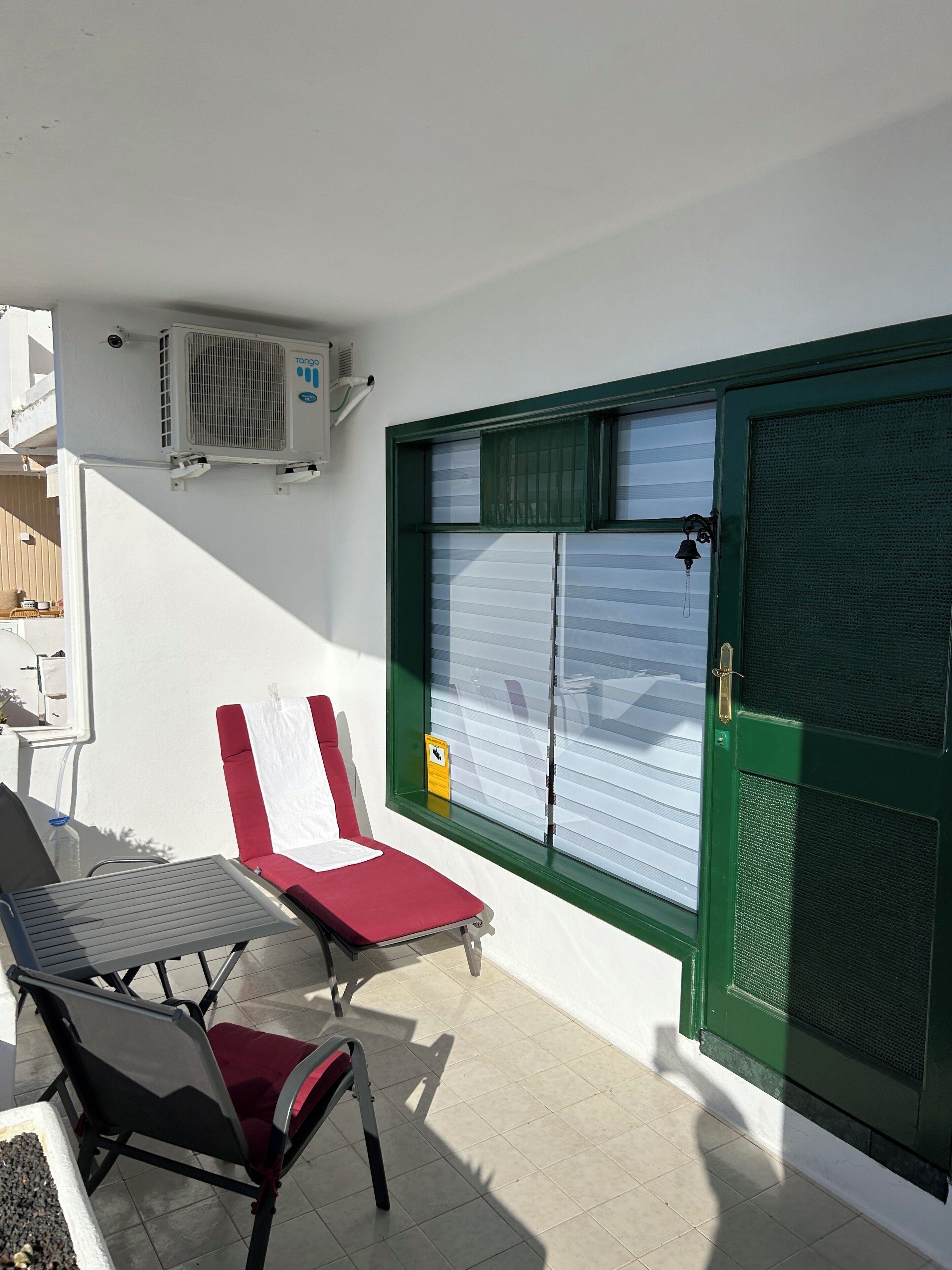 Un patio con dos sillones, una mesa y una puerta verde con mosquitero.