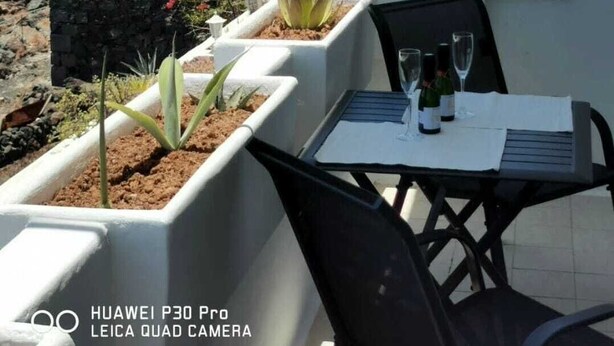 A terrace with a table and chairs, potted plants, and a view of a rocky hillside. - Pearl apartment - incredible view - in front of the ocean (Tías)