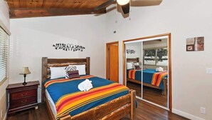 Une chambre à coucher avec un lit en bois, un ventilateur de plafond, un miroir et une table de chevet.