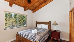 Un dormitorio con una cama de madera, una mesita de noche, una ventana con persianas y un techo de madera.