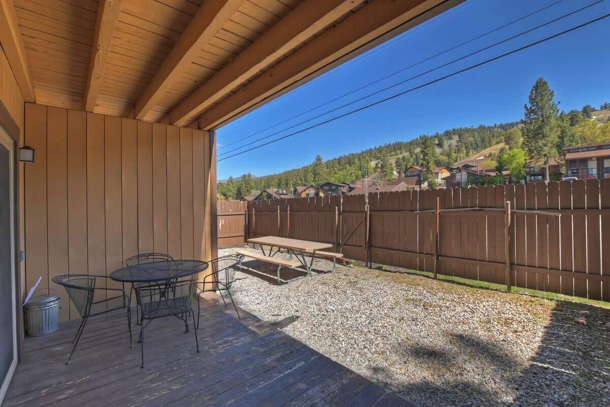 Un patio al aire libre con un suelo de madera, una mesa y sillas de metal, y una mesa de picnic.