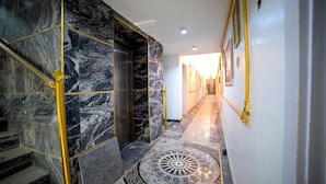 Een hal met marmeren vloer, een vloerkleed met patroon, een trap met gouden leuningen en een deur naar een andere kamer.