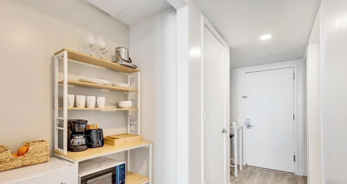 A modern kitchen with white cabinetry, a coffee machine, and a shelf with cups and bowls.