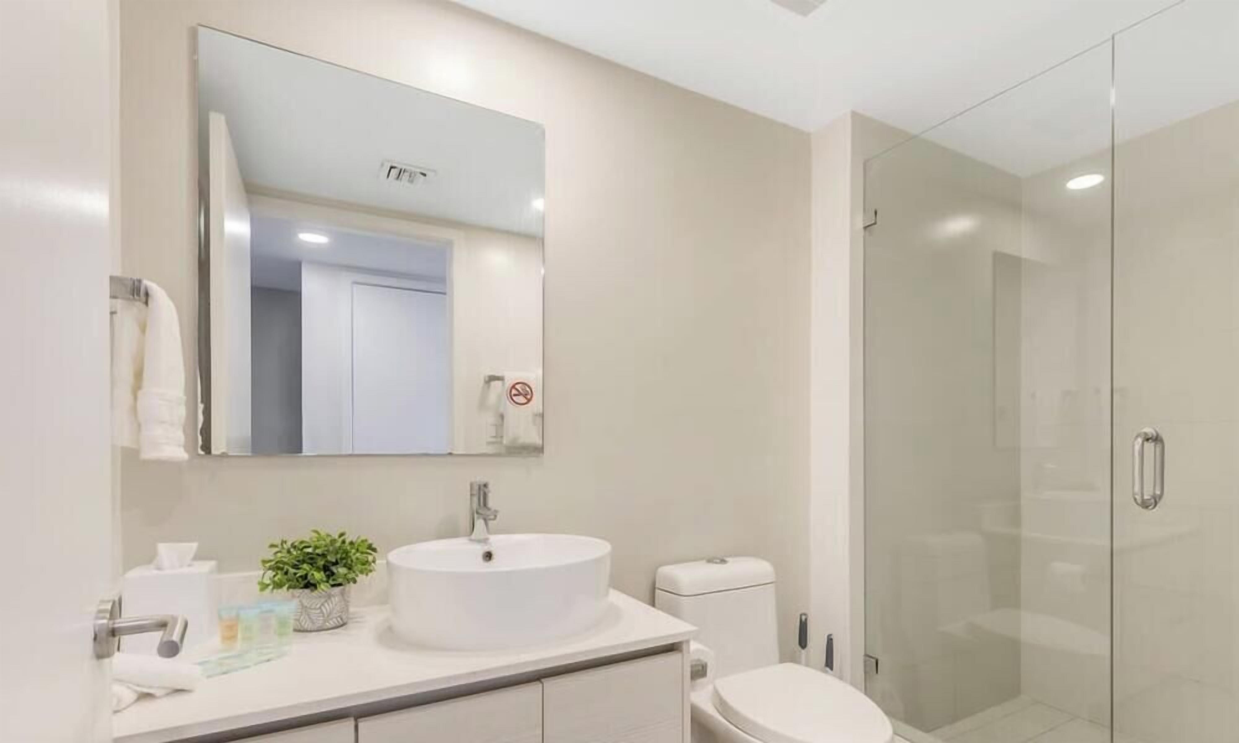 A modern bathroom with a large mirror, a round sink, a toilet, and a glass-enclosed shower.