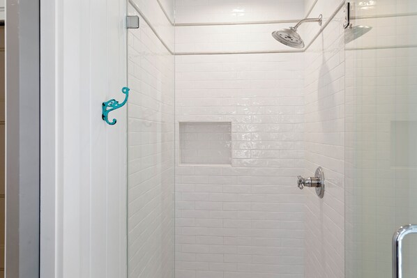 Un área de ducha pequeña y cerrada con paredes de azulejos blancos y una puerta de cristal.