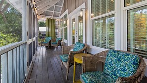 A covered porch with wicker furniture and a yellow table, large windows, and a view of greenery. - Goodnight Moon - Newly Renovated 30A Cottage in Historic Grayton Beach! (Grayton Beach)