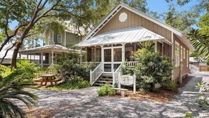 A two-story house with a porch, surrounded by trees and a gravel driveway. - Goodnight Moon - Newly Renovated 30A Cottage in Historic Grayton Beach! (Grayton Beach)