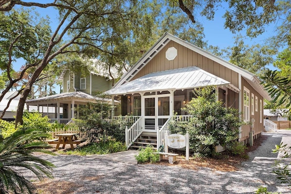 A two-story house with a porch, surrounded by trees and a gravel driveway.