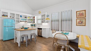 A compact kitchen with white cabinetry, a blue refrigerator, and a dining area with a wooden table and chairs. - Goodnight Moon - Newly Renovated 30A Cottage in Historic Grayton Beach! (Grayton Beach)