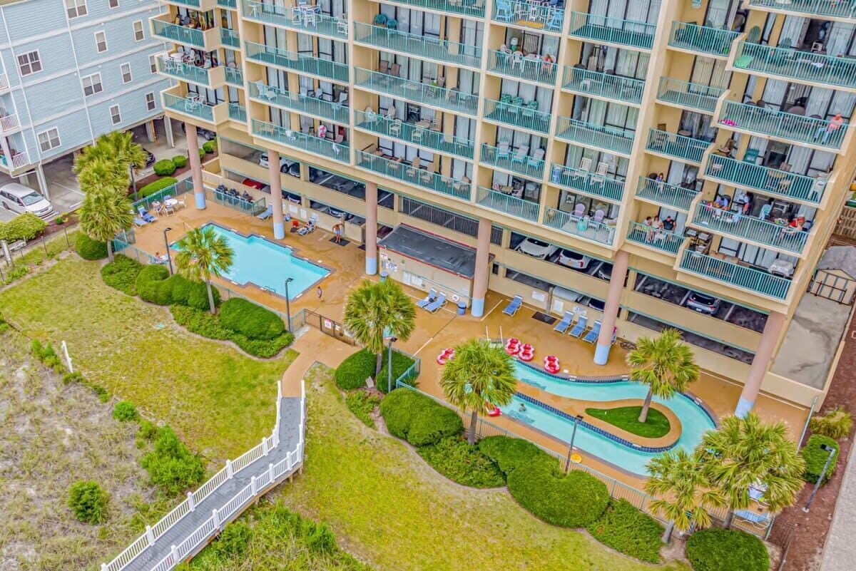 A multi-story hotel with balconies, a swimming pool, and a bridge.