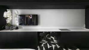 Una cocina moderna con una paleta de colores blanco y negro, un televisor de pantalla plana montado en la pared y una orquídea en maceta sobre la encimera.