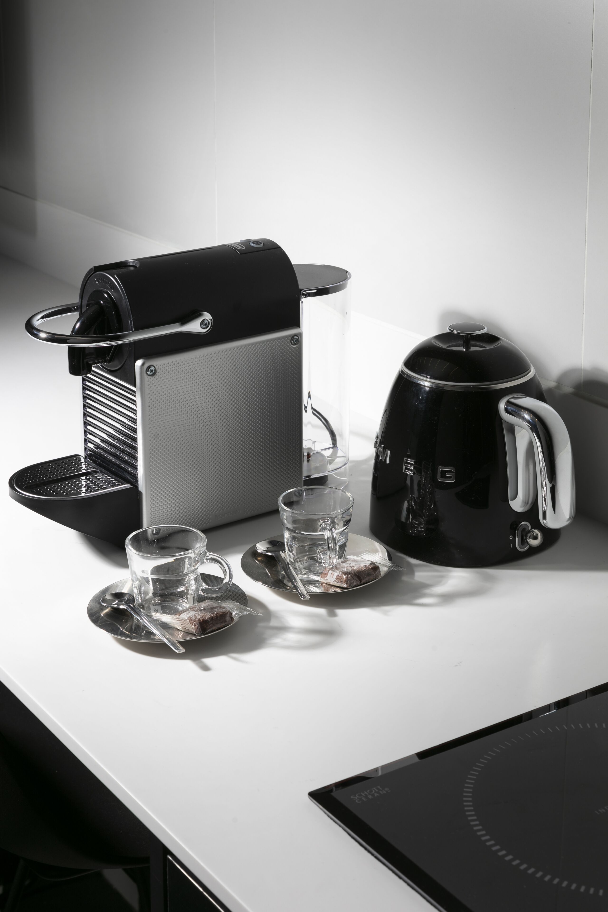A kitchen counter with a coffee maker, a kettle, and two cups with saucers.