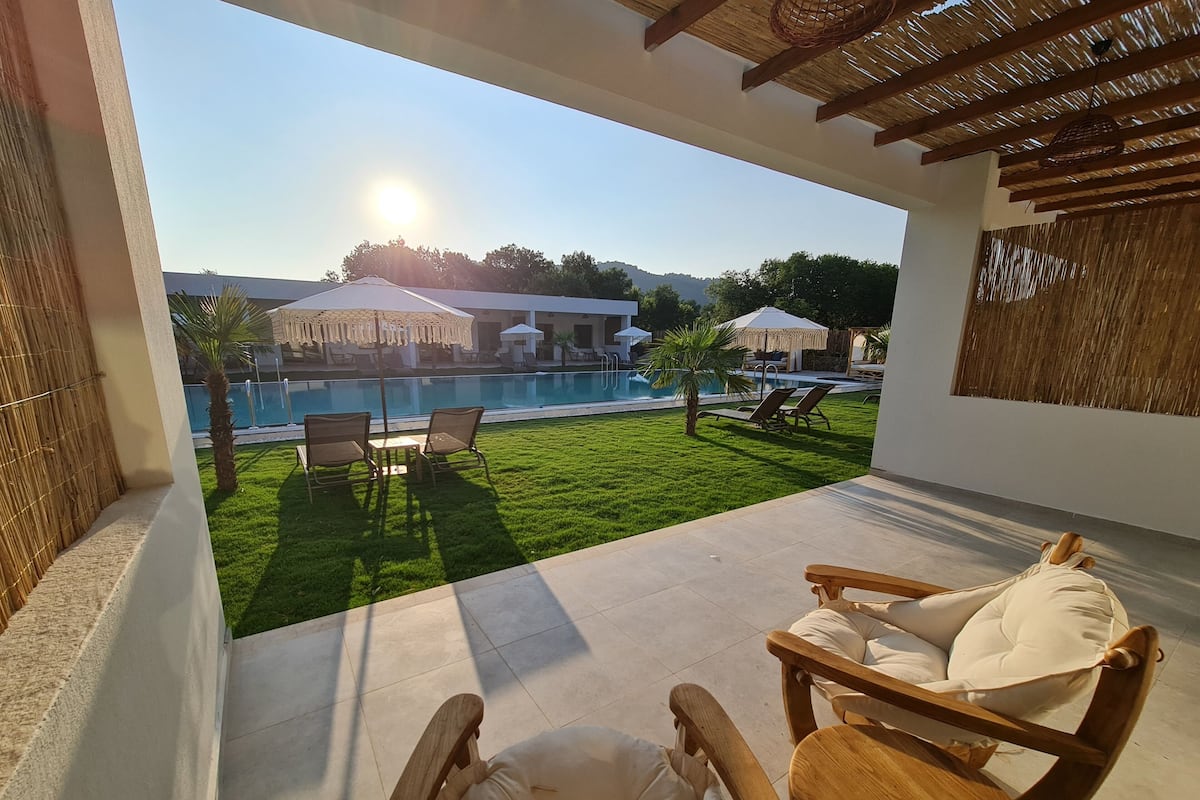 A patio with a view of a swimming pool, outdoor furniture, and a building in the background.