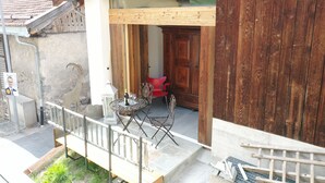 A wooden building with a balcony, a table with chairs, and a red chair inside. - Cozy apartment with high comfort for max. 6 people TIP bookable from 27.12.2025  (Schmitten)