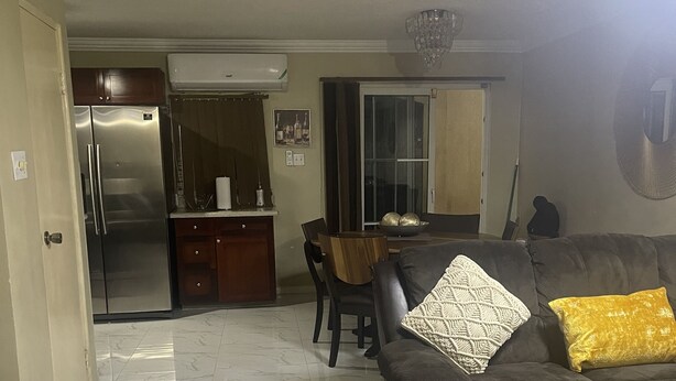 A living room with a sofa, a coffee table, and a dining area with a table and chairs. - This property is located in a quiet family oriented gated community in Portmore. (Portmore)