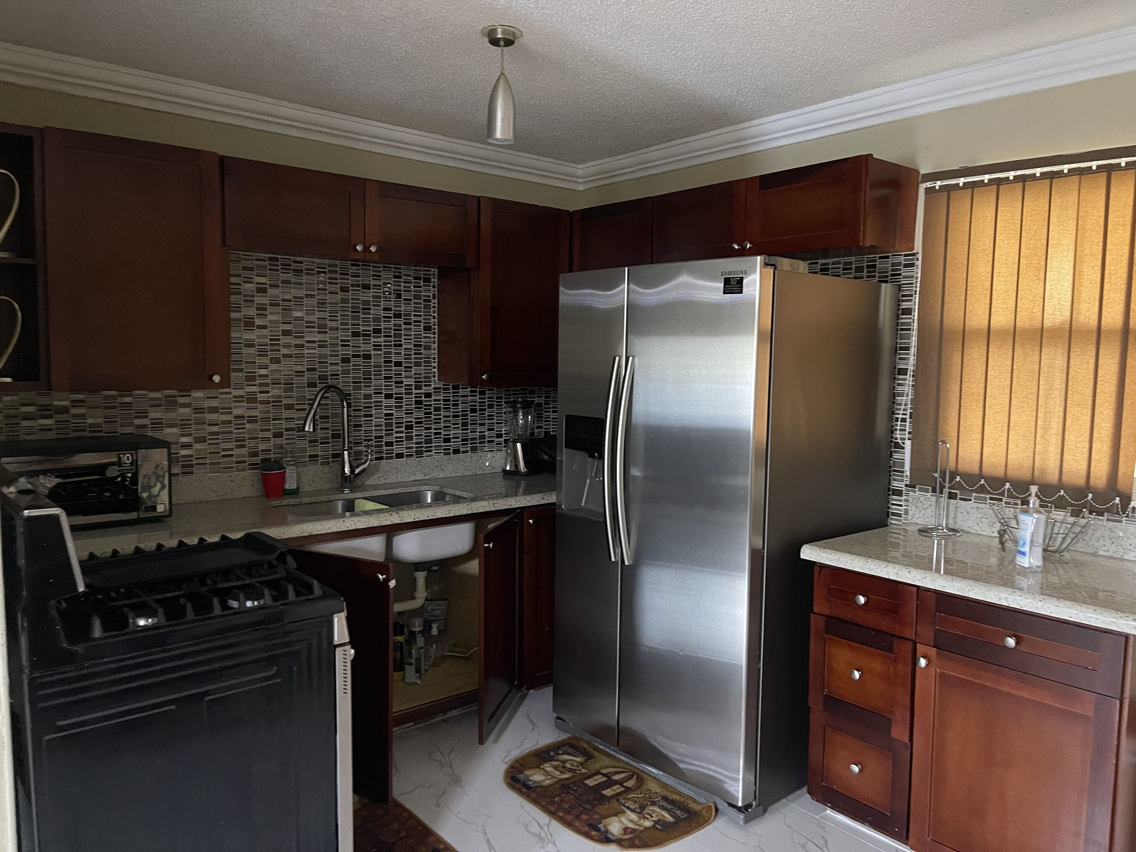 A kitchen with wooden cabinets, a stainless steel refrigerator, a microwave, and a tiled backsplash.
