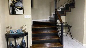 A staircase with dark wooden steps and black railings, leading to an upper floor. - This property is located in a quiet family oriented gated community in Portmore. (Portmore)