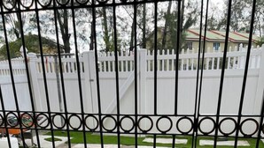 A gated courtyard with a geometric lawn design, a white picket fence, and a stone pathway. - This property is located in a quiet family oriented gated community in Portmore. (Portmore)