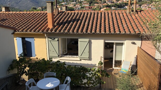 A residential building with a tiled roof, a balcony with a table and chairs, and a view of a hillside town. - Renovated house, Collioure near center, mountain views, quiet (Collioure)