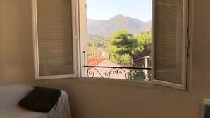 A room with a bed, a wooden table, a chair, and a window with open shutters. - Renovated house, Collioure near center, mountain views, quiet (Collioure)