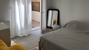 A bedroom with a bed, a bedside table, a mirror, and a view of an outdoor area with a wooden fence and plants. - Renovated house, Collioure near center, mountain views, quiet (Collioure)