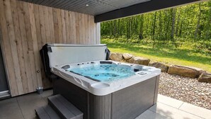 A modern outdoor hot tub with steps leading up to it, surrounded by a wooden wall and a covered area with a view of a bamboo forest. - Bright Cottage - 3 min from Tremblant North Slope (Lac-Supérieur)