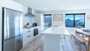 A modern kitchen with a stainless steel refrigerator, white cabinetry, and a large island with a sink. - Tranquil Heights Wanaka (Wānaka)