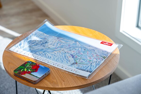 A wooden table with a large map, a stack of coasters, and a small book. - Tranquil Heights Wanaka (Wānaka)