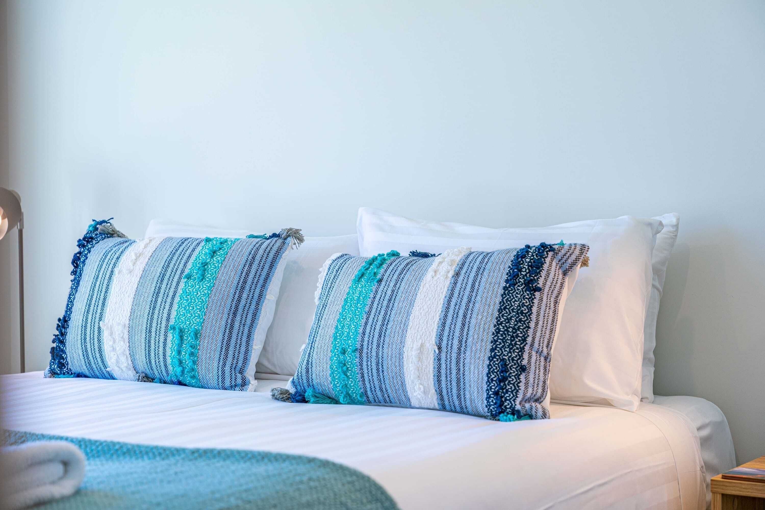 Uma cama com roupa de cama branca e almofadas listradas.