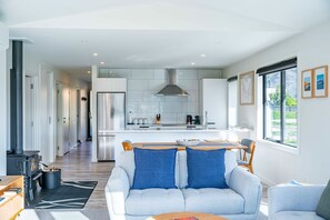 A modern kitchen with white cabinets, a stainless steel range hood, and a dining area with a light blue sofa and wooden table.