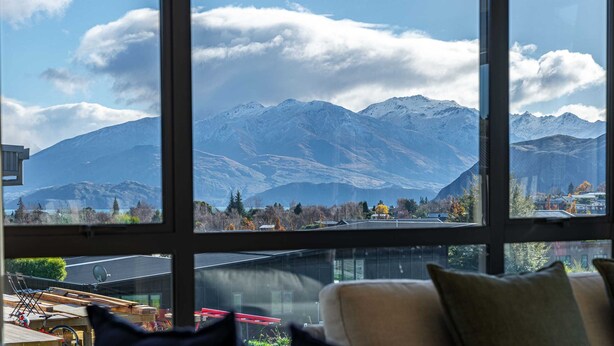 A room with a large window offering a view of snow-capped mountains and a clear sky. - Tranquil Heights Wanaka (Wānaka)