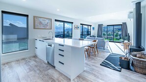 A modern kitchen with a large island, a dining area with a view, and a living space with a fireplace. - Tranquil Heights Wanaka (Wānaka)
