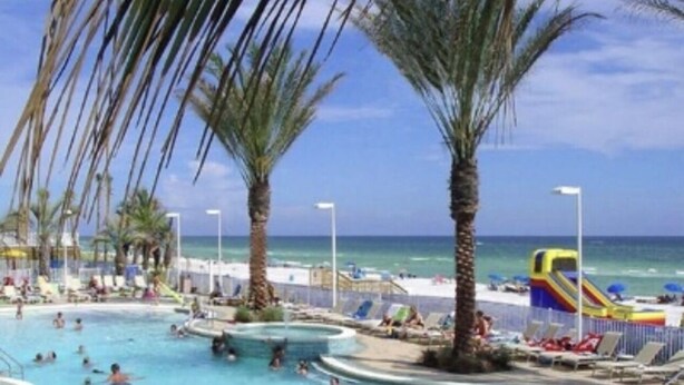 Un espace piscine comprenant plusieurs zones de baignade, des palmiers et une plage en arrière-plan.