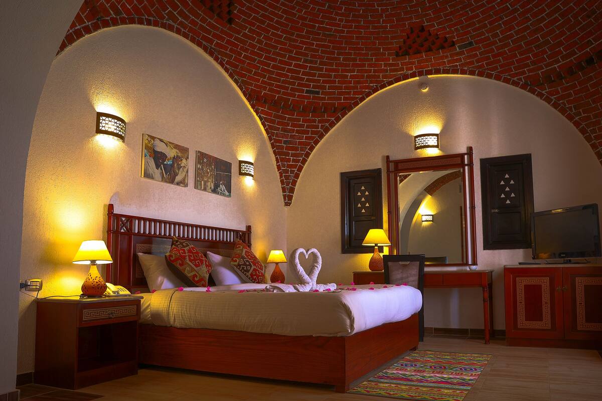 Ein Hotelzimmer mit Ziegeldecke, einem Bett mit gemusterten Kissen, einem Schreibtisch mit Lampe und einem Fernseher.