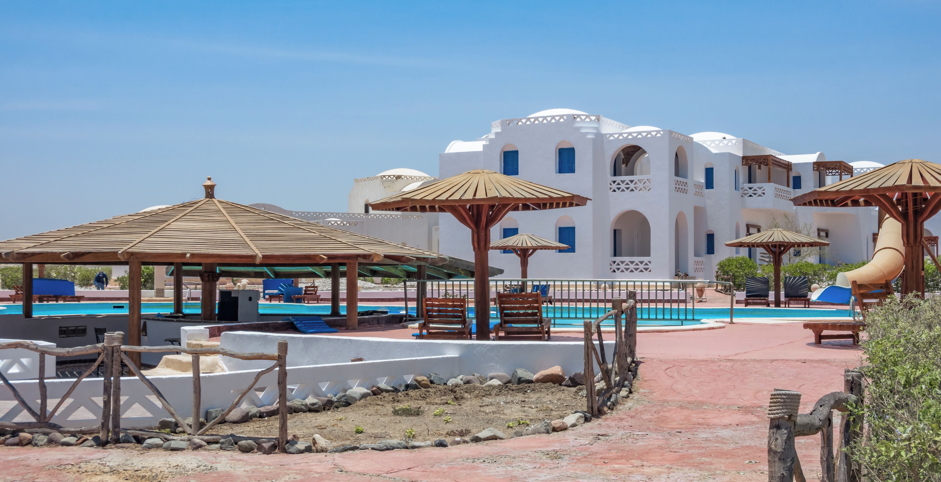 A resort with a pool, wooden gazebos, and a white building with arches.