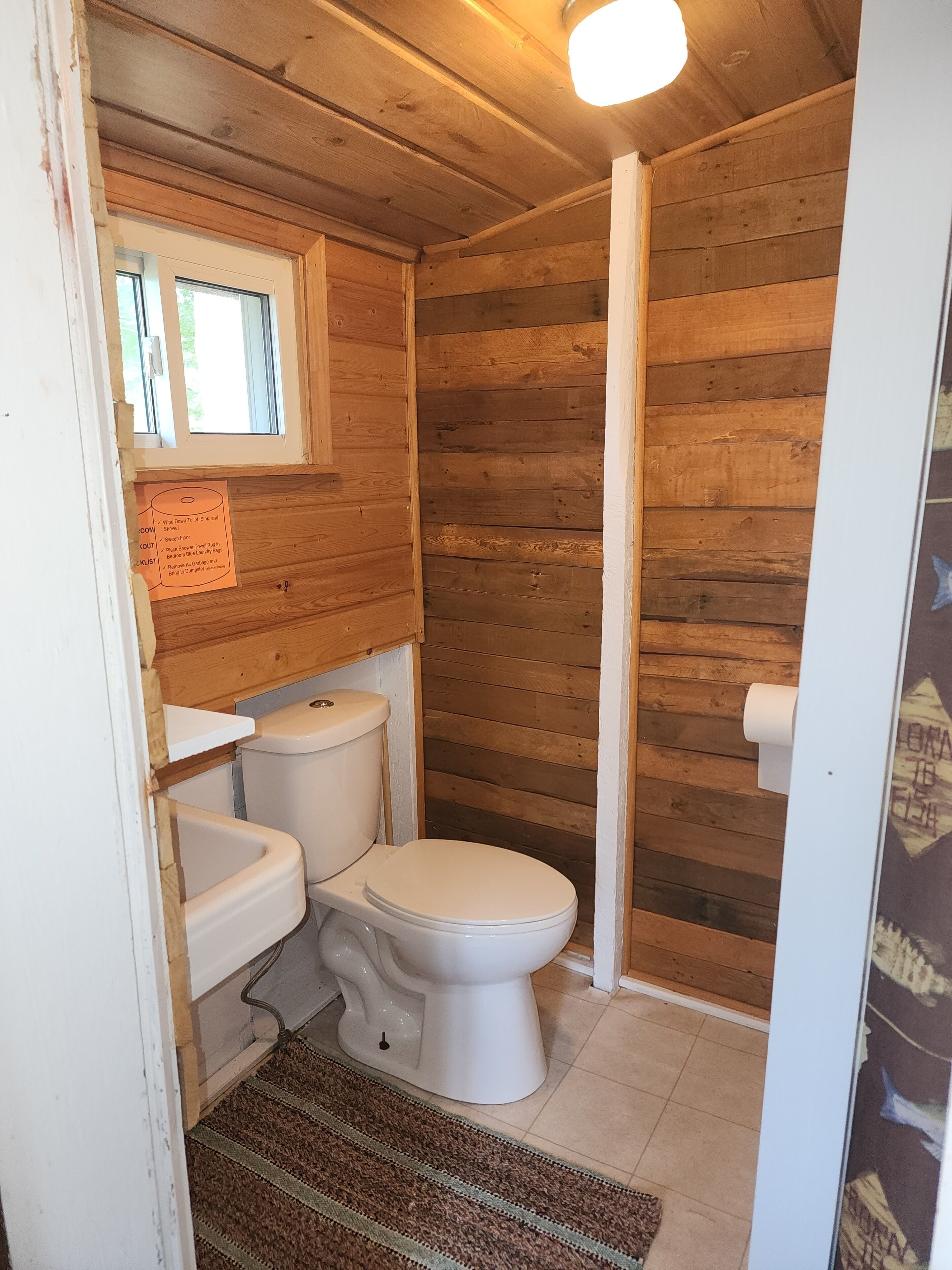 A compact wooden bathroom with a toilet, sink, and a window.
