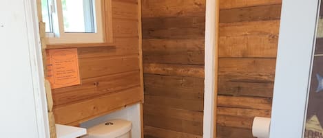 A compact wooden bathroom with a toilet, sink, and a window.