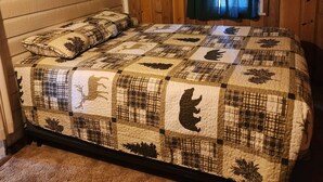 Un dormitorio con techo de listones de madera, colcha acolchada con estampados de animales, una ventana con cortinas y pared de madera.