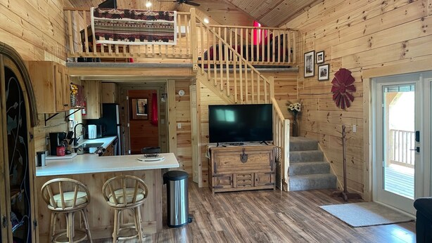 Interior de una cabaña con cocina, comedor y escalera a un entrepiso.