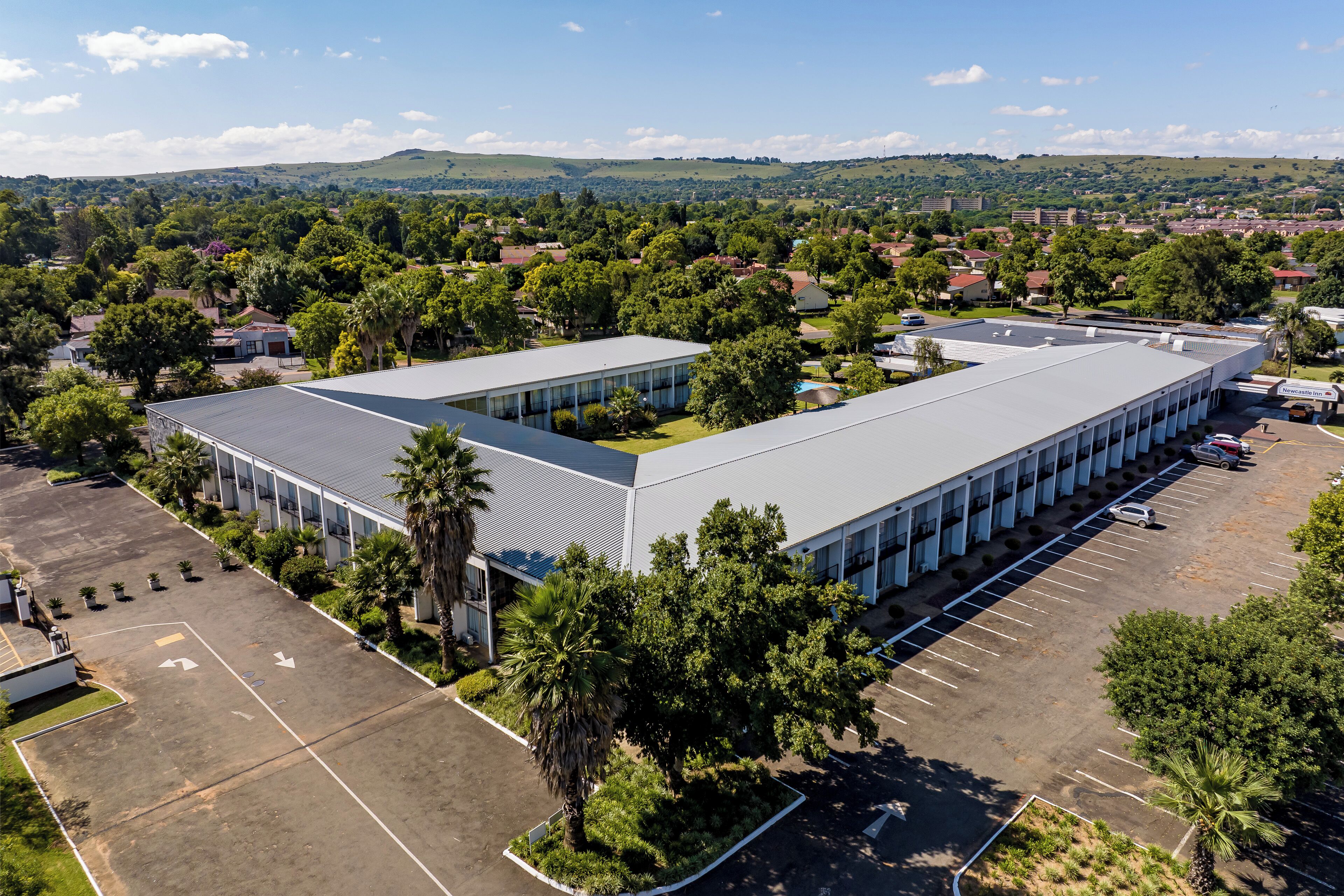 A large industrial building with a flat roof, surrounded by parking and greenery.