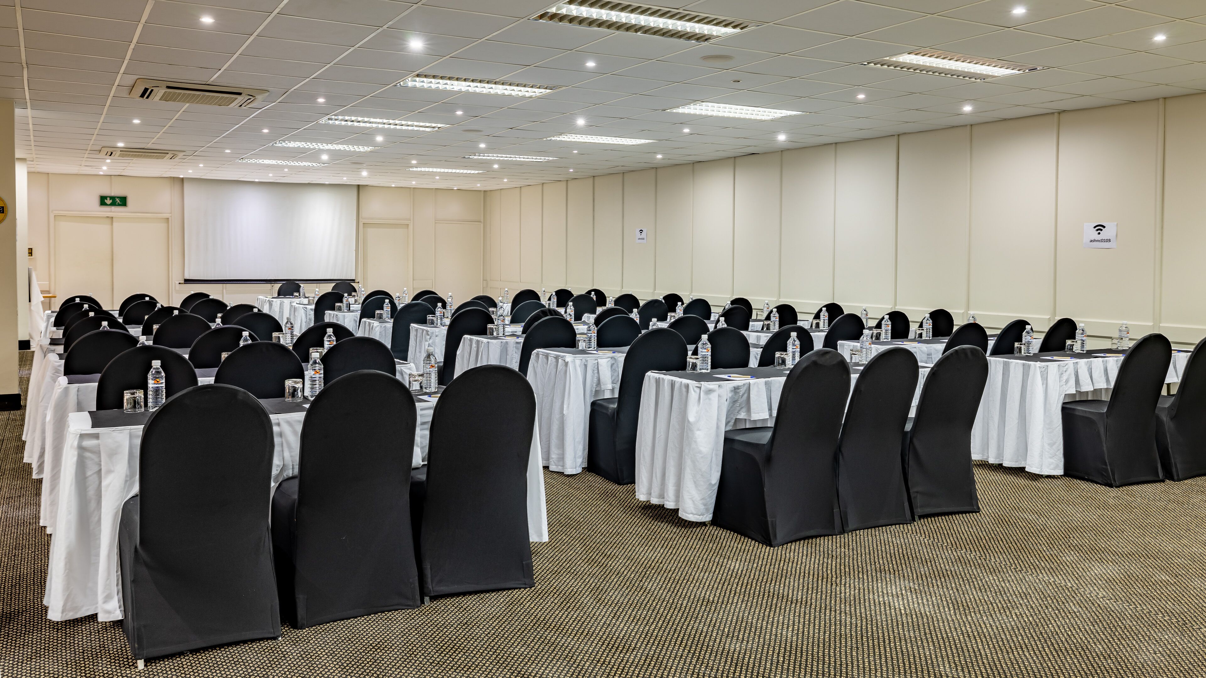 A conference room with rows of tables and chairs, equipped with water bottles and nameplates.