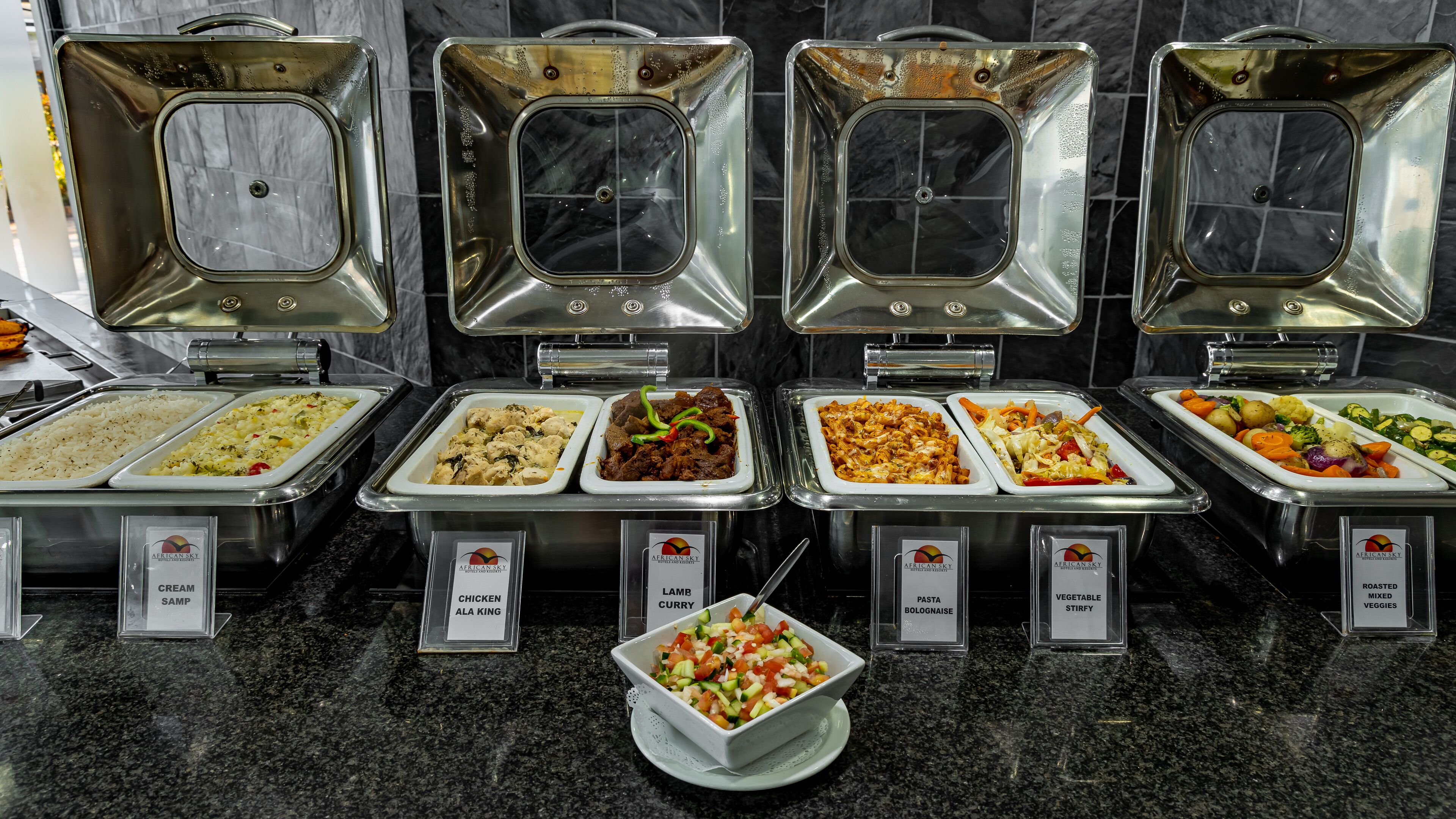 A buffet with labeled dishes including cream soup, chicken ala king, lamb curry, pasta bolognese, vegetable stir-fry, and roasted mixed veggies.