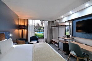 A hotel room with a bed, desk, chair, TV, and a view of the outdoors. - African Sky Hotels - Newcastle Inn (Newcastle)