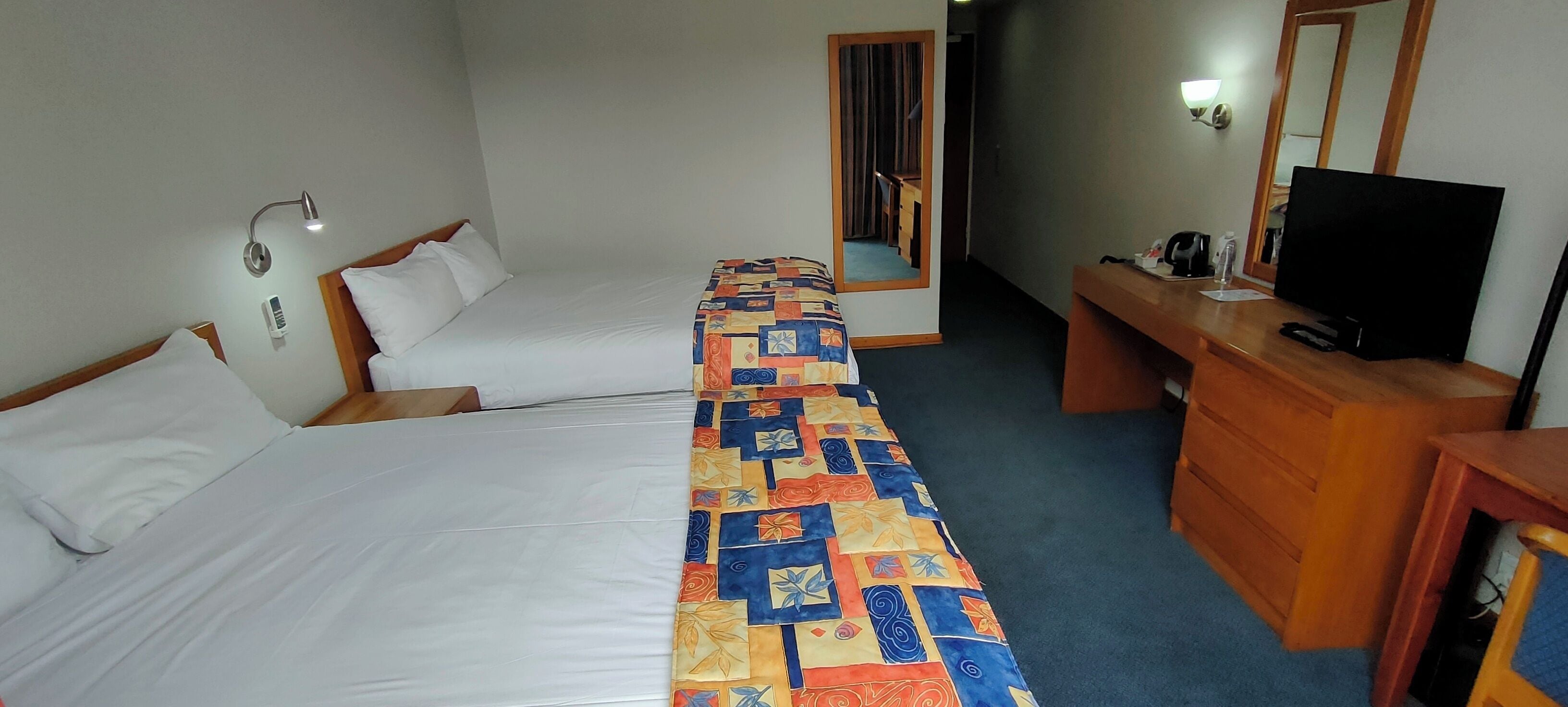 Een hotelkamer met twee bedden, een bureau, een televisie en een spiegel.