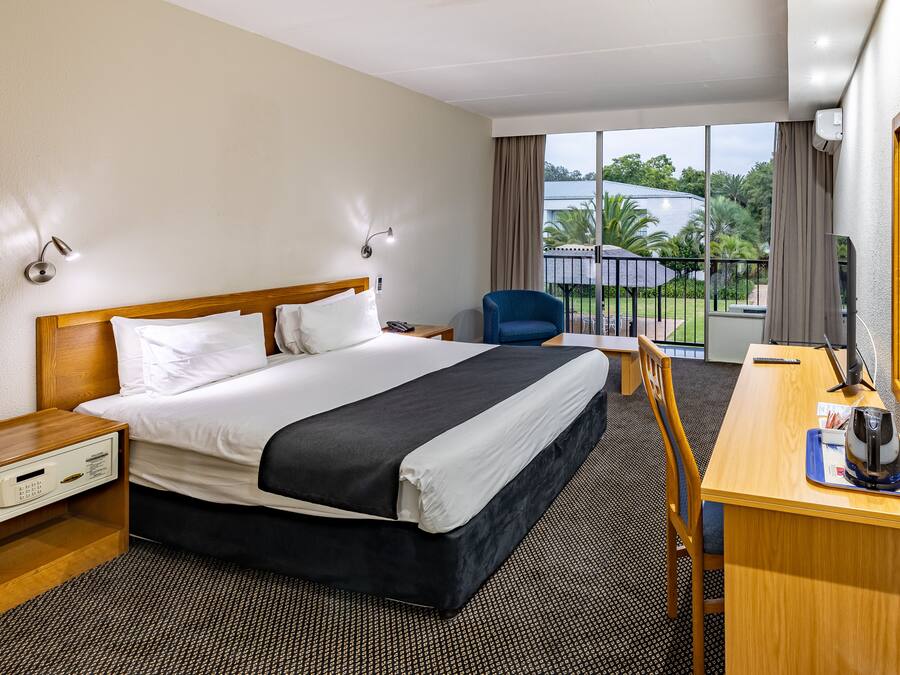 Une chambre d’hôtel comprenant un lit, des tables de chevet, un bureau avec une chaise, une machine à café et une vue sur l’extérieur.