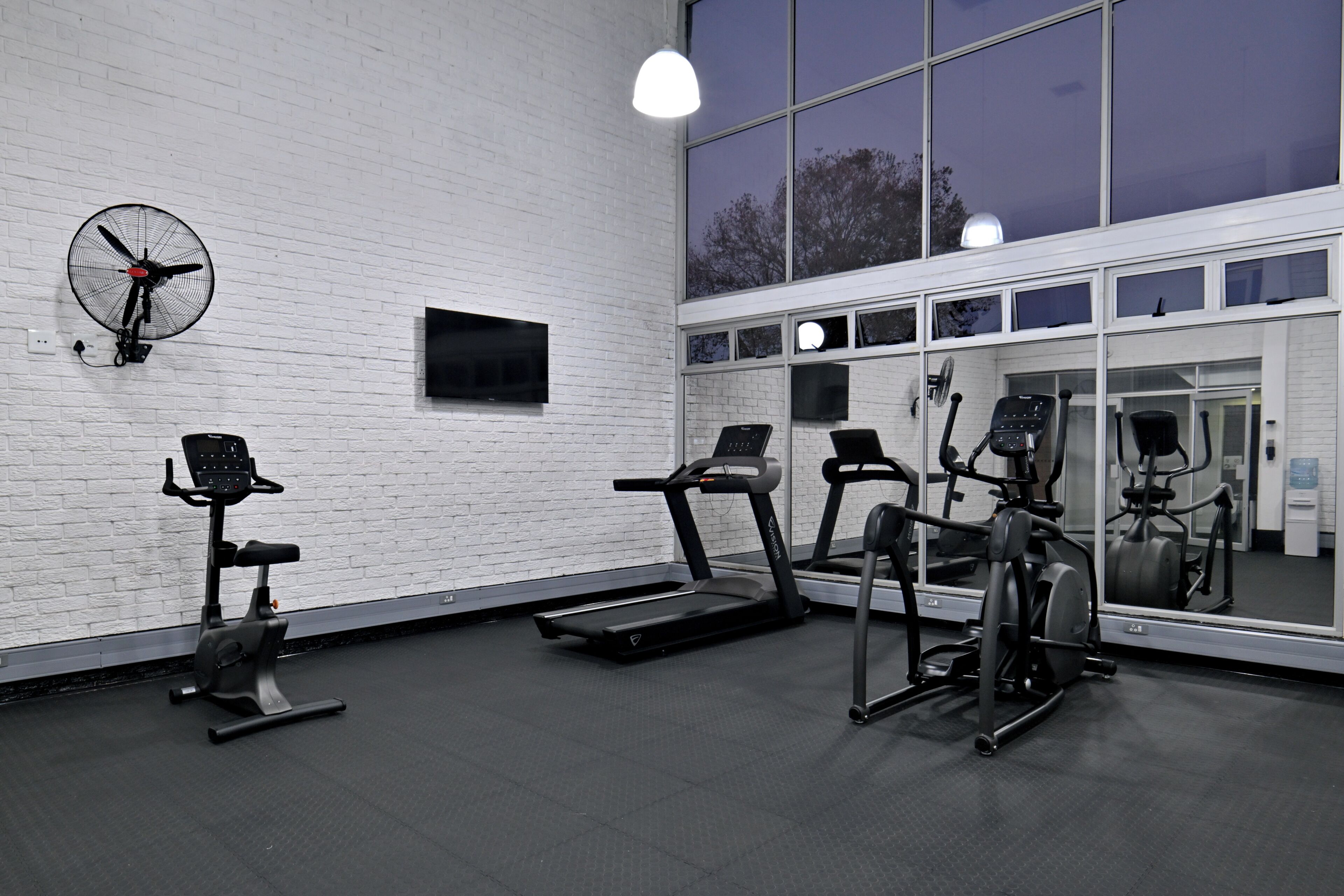 A gym with exercise equipment, a large mirror, and a white brick wall.